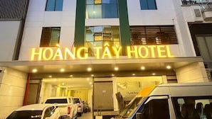 The exterior of Hoàng Tài Hotel with a modern design, featuring a prominent entrance and multiple vehicles parked in front.