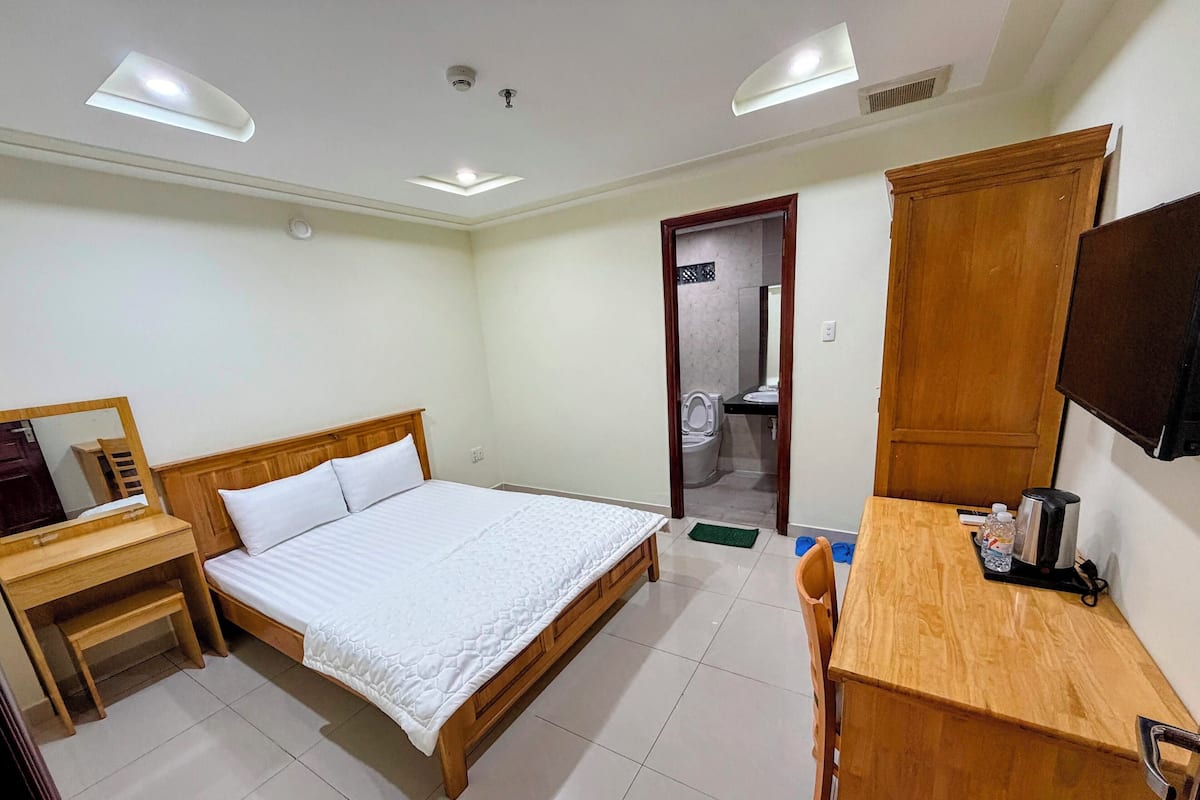 Habitación de hotel con cama y escritorio de madera, un espejo, armario y televisión.