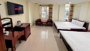 A hotel room with a TV displaying Netflix, a desk with a coffee maker, two armchairs, a bed, and a window with curtains.