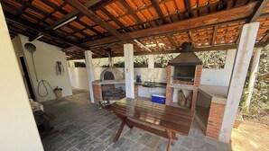 An outdoor kitchen area with a brick oven, a grill, and a wooden table. - Rancho dos Capelos (Nazaré Paulista)