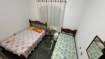 Quarto pequeno e compacto com duas camas de solteiro, cabeceira de madeira, uma mesinha e um espelho.