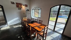 A dining area with a wooden table and chairs, a refrigerator, and a window with a view of the outdoors. - Rancho dos Capelos (Nazaré Paulista)