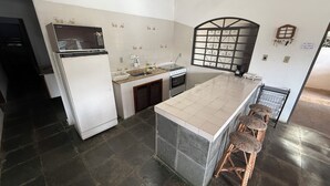 A compact kitchen with a refrigerator, stove, sink, and a small dining area with stools. - Rancho dos Capelos (Nazaré Paulista)