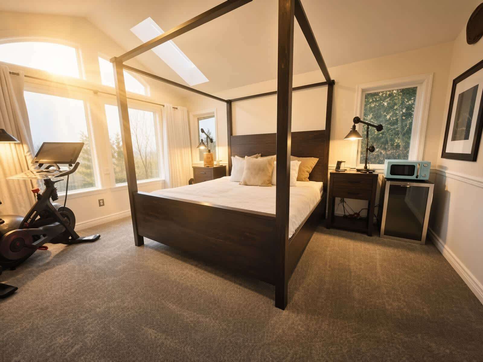 Ein Bett mit Baldachin, dessen dunkles Holzgestell einen kleinen Nachttisch mit Lampe, eine Mikrowelle und ein Fenster mit Vorhängen beherbergt.