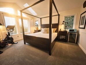 Ein Bett mit Baldachin, dessen dunkles Holzgestell einen kleinen Nachttisch mit Lampe, eine Mikrowelle und ein Fenster mit Vorhängen beherbergt.