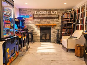 A room with a fireplace, a bookshelf, a claw machine, and a neon sign.