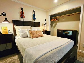 Un lit bien fait, recouvert d’une couverture matelassée, deux lampes de chevet, un livre d’or posé sur la table de chevet et un four à micro-ondes vintage sur une commode.