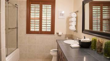 Ein Badezimmer mit Dusche, Toilette, Waschbecken und einem Fenster mit Jalousien.