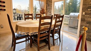 Un coin repas avec une table ronde, des chaises et une vue sur un patio équipé d’un barbecue.