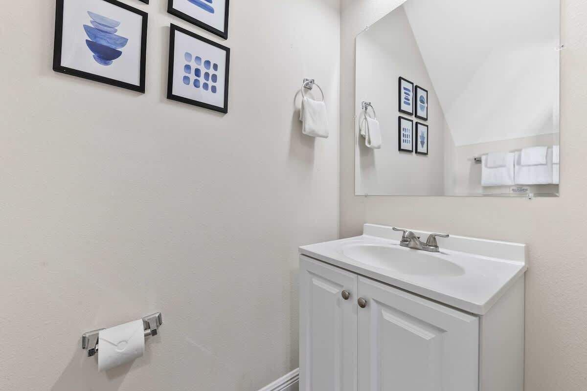A bathroom with a white sink, a mirror, and framed artwork on the wall.