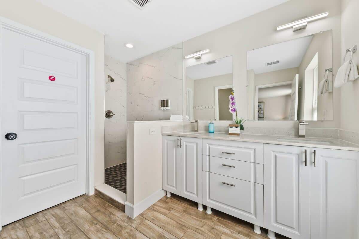Un baño moderno con un tocador blanco, un espejo grande y una zona de ducha.