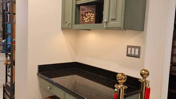 A kitchen with a green cabinet, a marble countertop, a stool, and a red rope barrier.