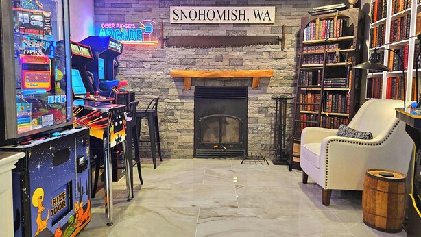 A cozy room with a fireplace, arcade games, and a bookshelf.