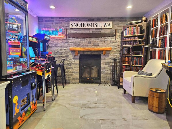 A cozy room with a fireplace, arcade games, and a bookshelf. - Private Bedroom w Hot Tub and Arcade (Snohomish)