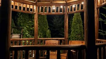 A wooden gazebo with a roof, surrounded by a wooden deck and chairs.