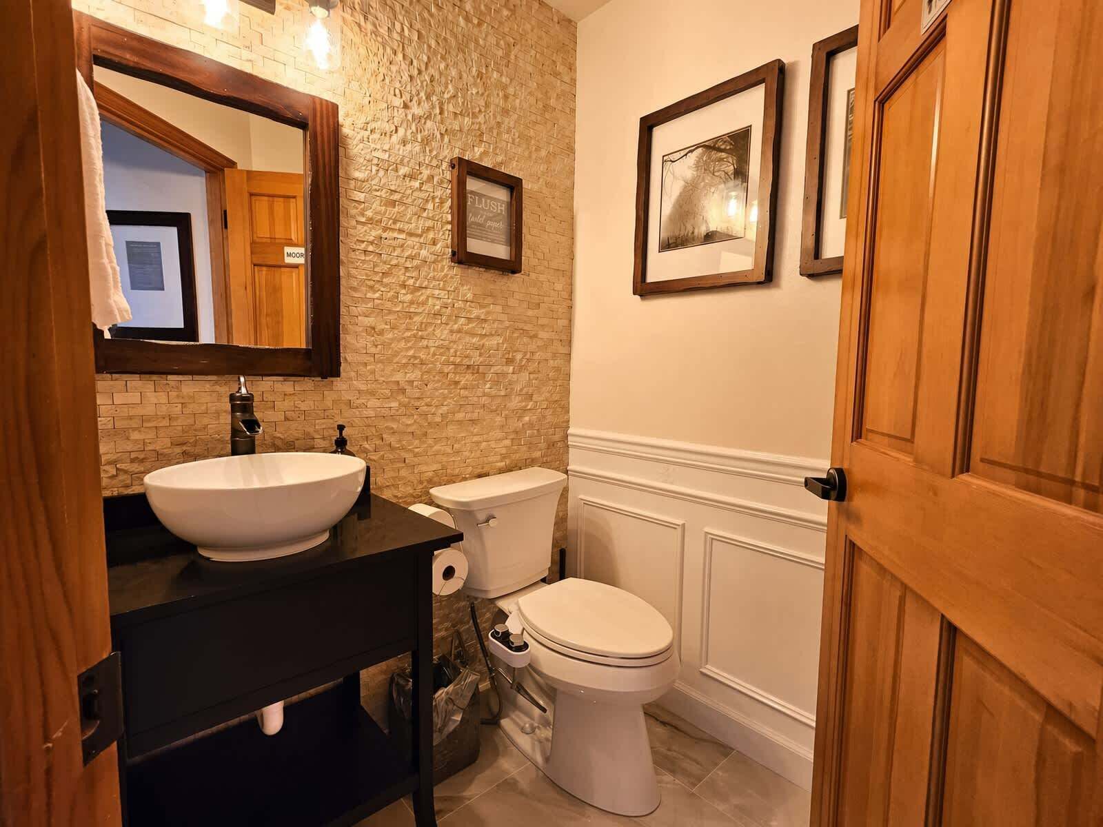 A bathroom with a white sink, a toilet, a mirror, and framed pictures on the wall.