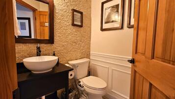 A bathroom with a white sink, a toilet, a mirror, and framed pictures on the wall.