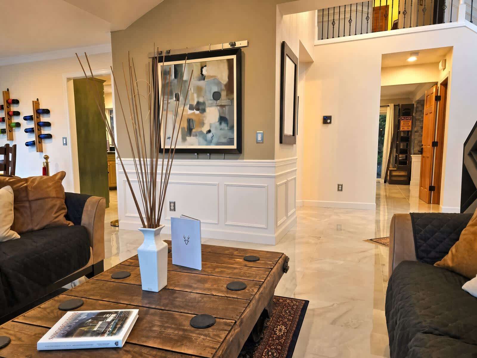 A modern living room with a wooden coffee table, a vase with sticks, and a framed abstract painting on the wall.