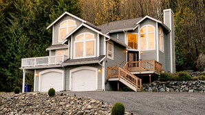 Une maison à deux étages, avec des fondations en pierre, un balcon et un garage.