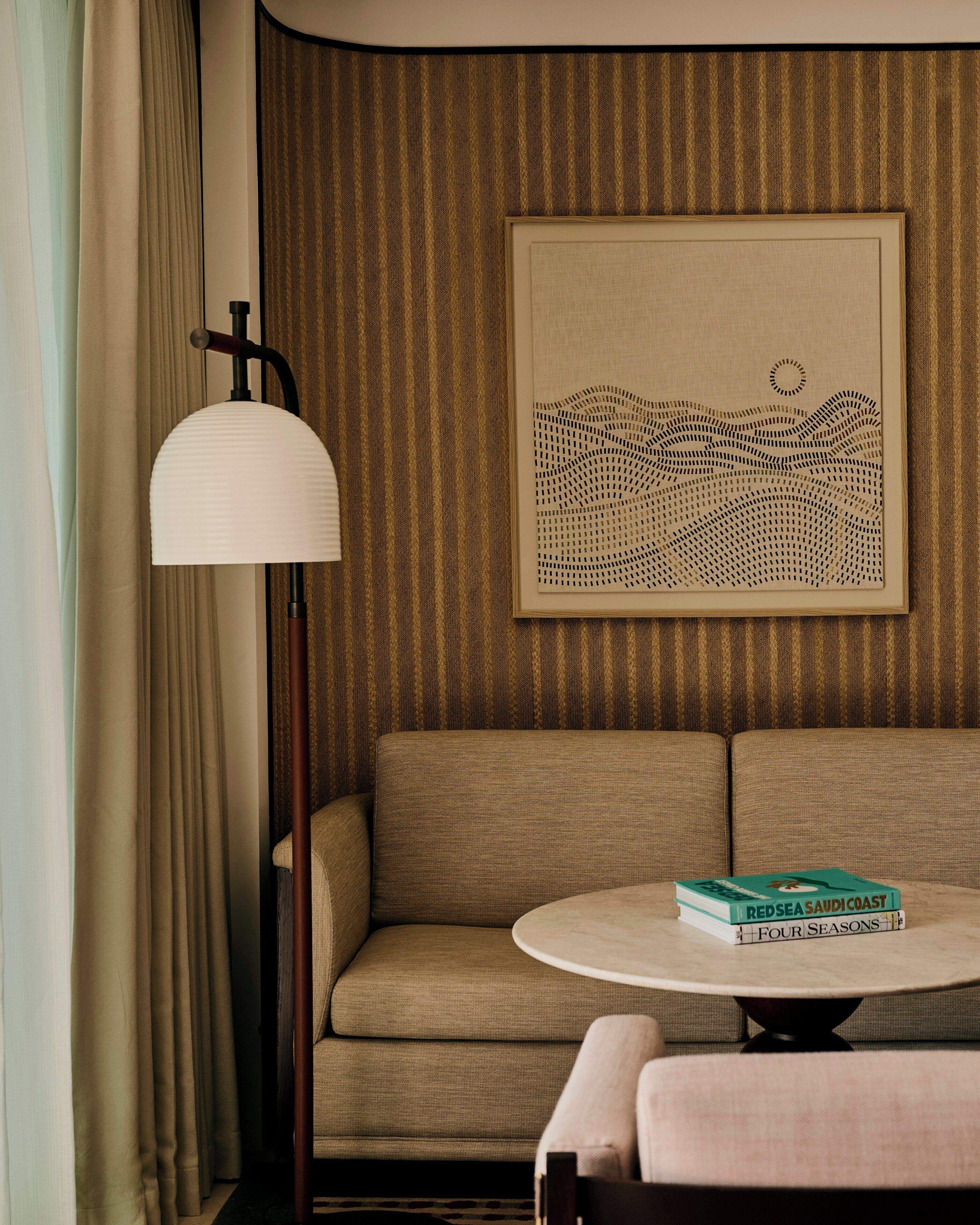 A hotel room with a sofa, a round table, a lamp, and a framed artwork on the wall.