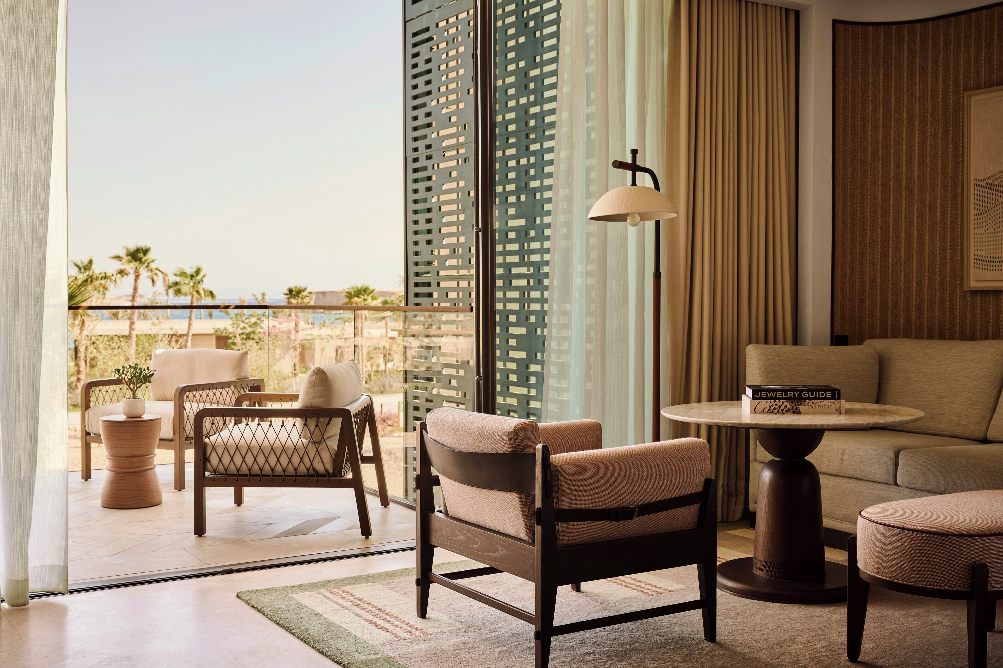 A room with a sofa, armchairs, a table, and a view of the beach.