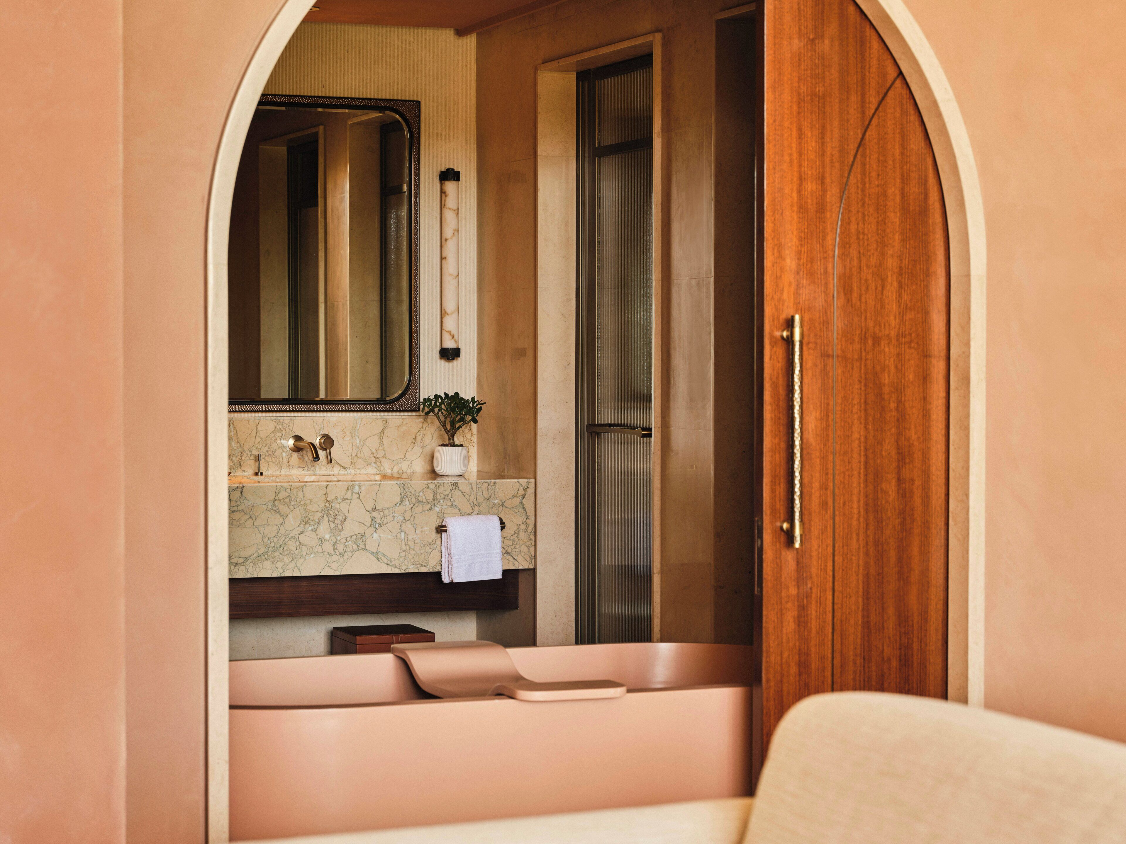Un baño con lavamanos de mármol, un espejo, una toalla y una puerta de madera.