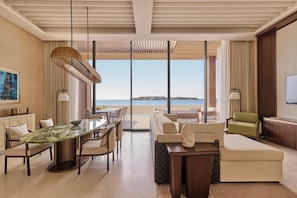 A modern hotel room with a dining area, a sofa, and a view of the beach.