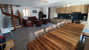 Amplia sala de estar con una escalera de madera, una mesa de comedor con sillas, una cocina con armarios de madera y un ventanal grande.