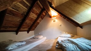 Un dormitorio acogedor en el ático, con dos camas individuales, vigas de madera y techo inclinado.