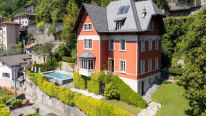Una casa a più piani con piscina, immersa nel verde e circondata da colline.