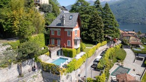 Una casa rossa con piscina, immersa nel verde e affacciata su un lago.