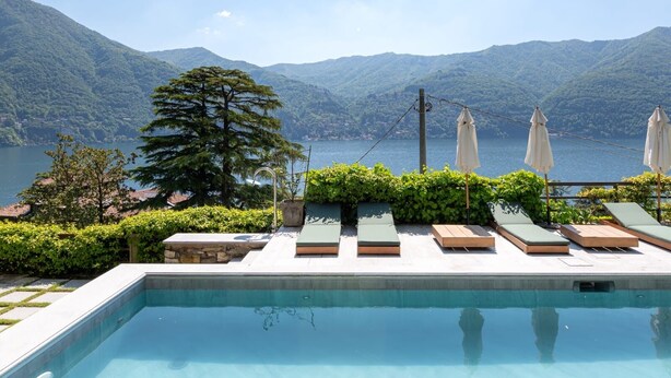 Piscina con lettini e ombrelloni con vista su un lago e montagne.