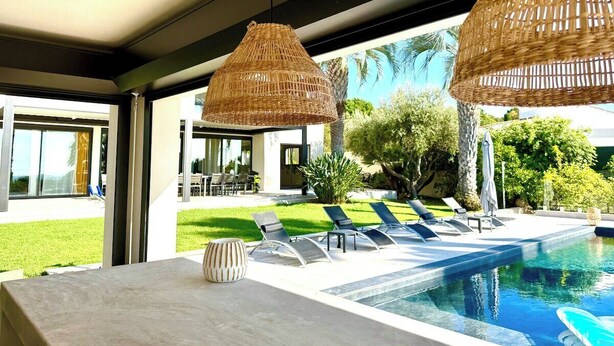 Un área de piscina moderna con sillones de descanso y una gran lámpara colgante de mimbre.