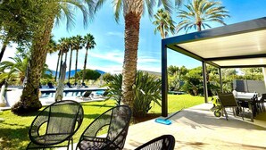 Un área de piscina con sillones de descanso, un porche cubierto y palmeras.