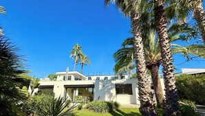 Una casa moderna de fachada blanca, rodeada de abundante vegetación y palmeras.