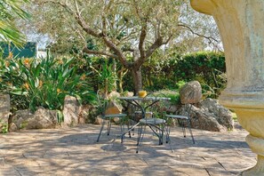 Un espace extérieur aménagé en terrasse, avec une table en pierre et des chaises en métal, entouré de rochers et de verdure.