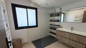 Moderni kylpyhuone, jossa on lasinen suihkuseinä, suuri ikkuna ja peilillä varustettu pesuallas.