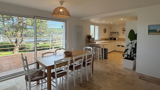 Una cocina amplia con un gran ventanal, un comedor con mesa de madera y sillas blancas, y una lámpara colgante.