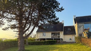 Una casa de dos pisos con un balcón, rodeada de un césped cuidado y un árbol grande.