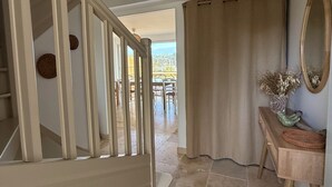 Una escalera con barandilla de madera, una lámpara de techo tejida, una consola de madera con espejo y vistas a un patio exterior.