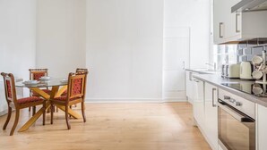 A modern kitchen with white cabinets, a built-in oven, and a dining area with a glass table and wooden chairs. - Main Door Private Entrance Apartment (Edinburgh)