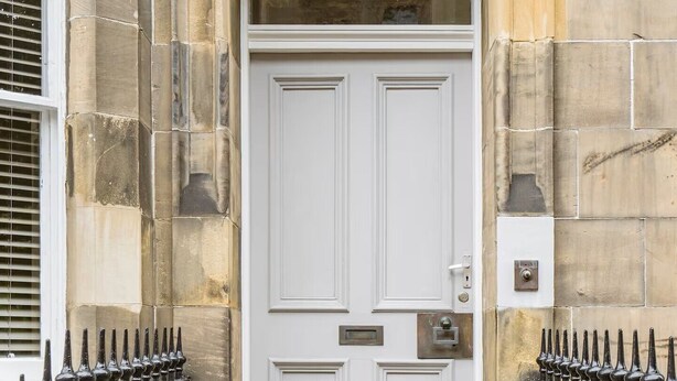 A white door with a number plate, flanked by black iron railings, leading to a stone building entrance. - Main Door Private Entrance Apartment (Edinburgh)