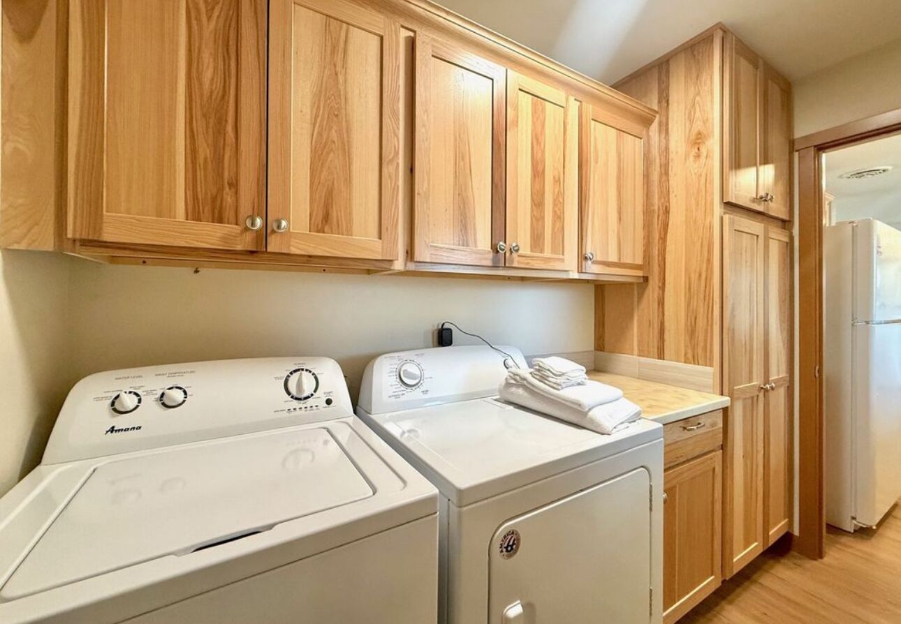 A laundry area with two washing machines, wooden cabinets, and a countertop.