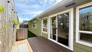 Eine Holzterrasse mit einem weißen Haus, Schiebeglastüren und einem Holzzaun.