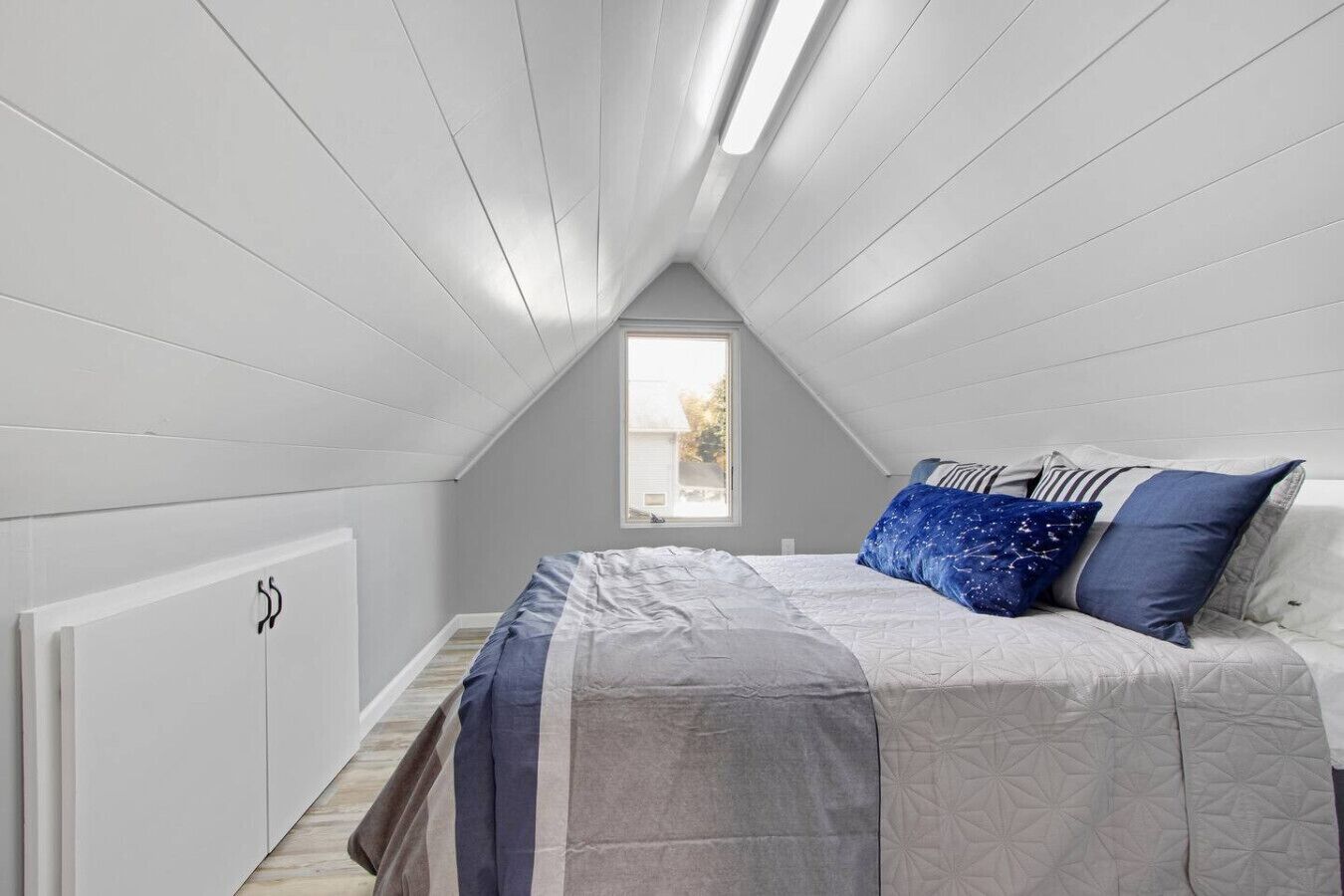 A bedroom with a sloped ceiling, a window, a bed with a patterned bedspread, and a radiator.