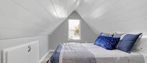 A bedroom with a sloped ceiling, a window, a bed with a patterned bedspread, and a radiator.