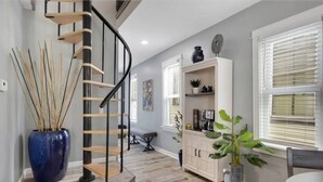 Un intérieur moderne avec un escalier en colimaçon, un plancher en bois, un coin repas avec une table et des chaises, et un meuble contenant des objets décoratifs.