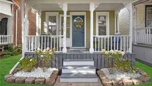 Une maison à deux étages avec un porche à l’avant, une porte bleue et une guirlande décorative.