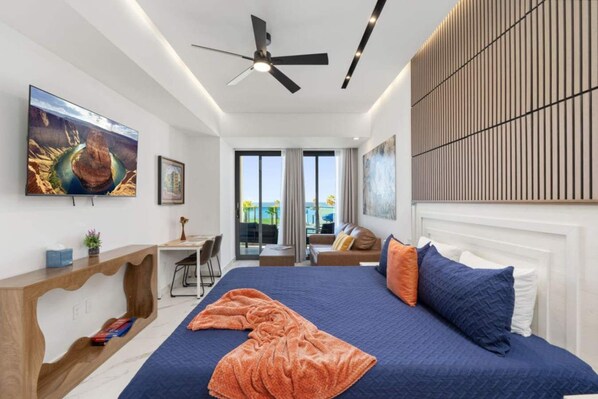 A modern hotel room with a large bed, a desk, and a balcony with a view of the ocean. - Encantame Soleil studio lock off sleeps 4 (Playa Encanto)