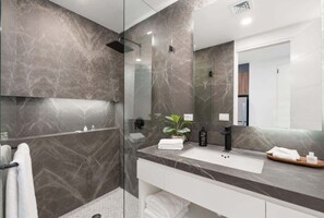 A modern bathroom with a glass-enclosed shower, marble walls, and a white vanity with a mirror. - Encantame Soleil studio lock off sleeps 4 (Playa Encanto)